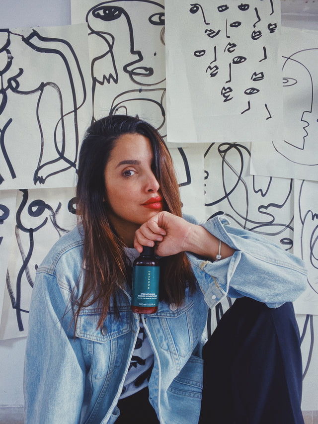Woman with long brown hair wearing denim jacket holding blue bottle of scalp conditioner