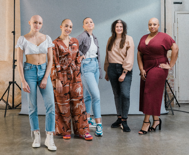 Group of five diverse women in casual and elegant outfits posing against a grey backdrop indoors