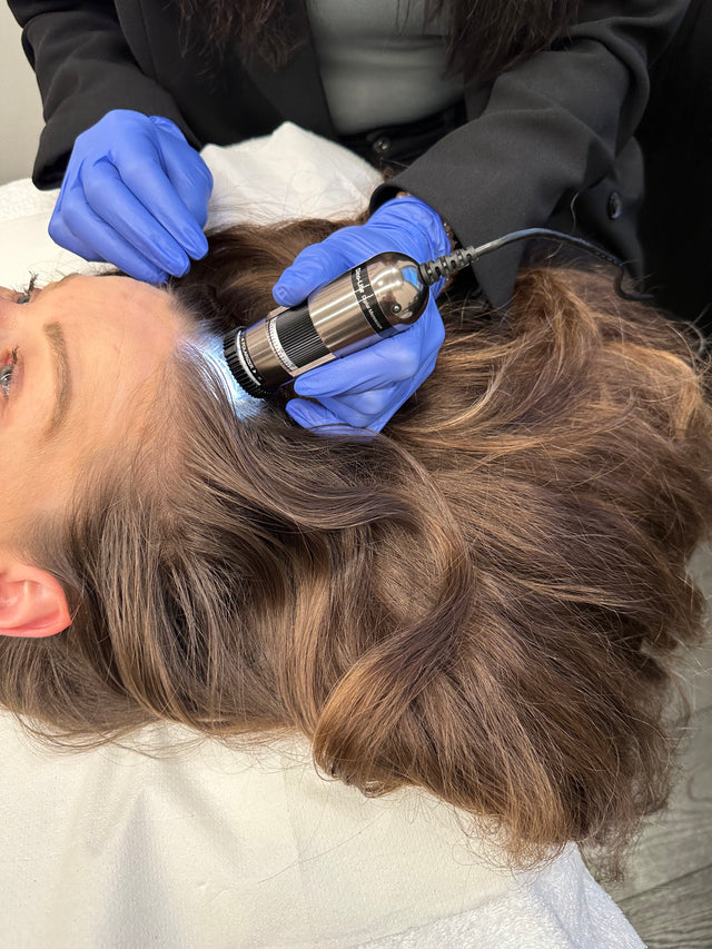 Person receiving scalp examination with handheld magnifying device by gloved professional