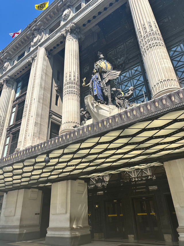 Grand entrance of Selfridges & Co. with classical columns and ornate statue under glass canopy