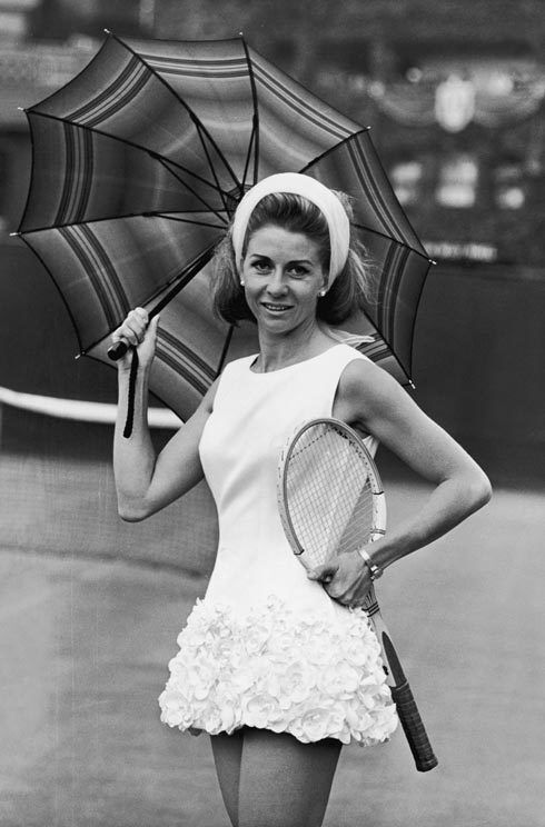 Woman in white sleeveless dress with floral skirt holding tennis racket and striped umbrella