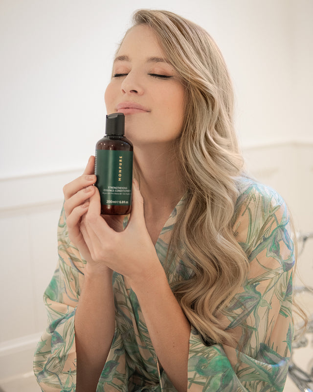 Woman with long blonde hair holding a brown bottle of Monpure strengthening essence conditioner