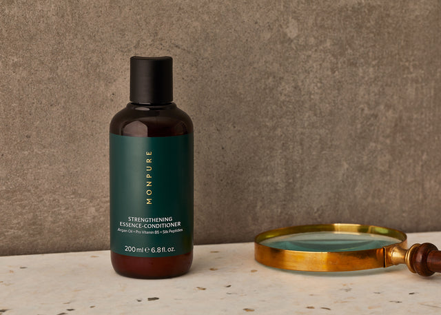 Brown bottle of Monpure Strengthening Essence-Conditioner with green label and black cap on marble surface