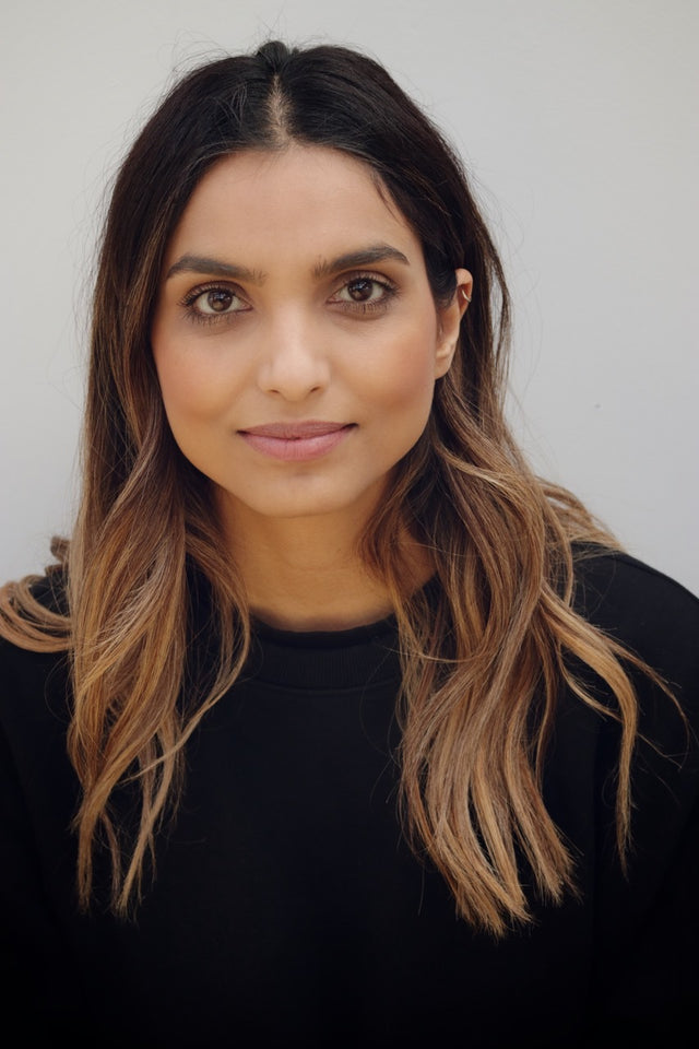 Woman with long brown hair wearing a black top against a plain light background