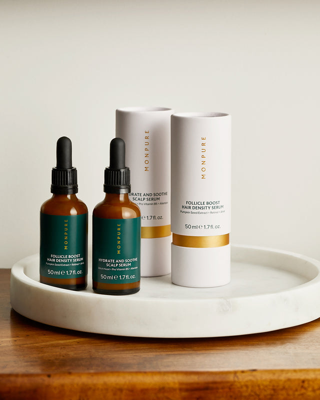 Two amber glass dropper bottles and two white cylindrical boxes of Monpure scalp serums on a white marble tray