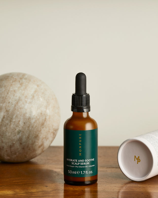 Amber glass bottle with black dropper cap containing Monpure Hydrate and Soothe scalp serum on wooden surface