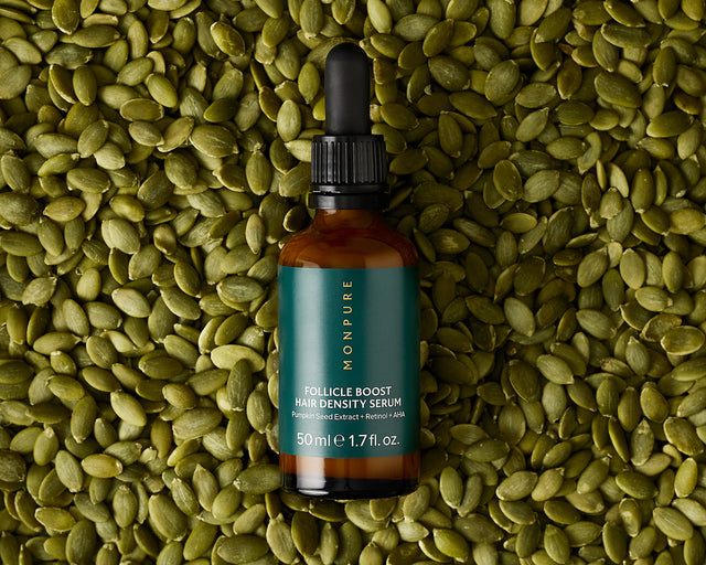 Amber glass bottle of MONPURE Follicle Boost Hair Density Serum with green label on pumpkin seeds background
