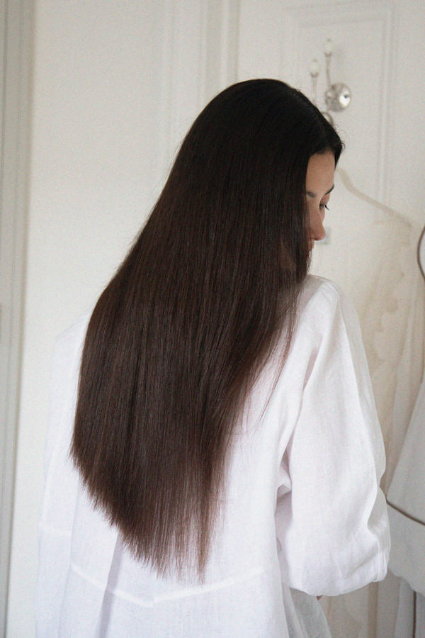 Woman with long, straight dark brown hair wearing a loose white shirt indoors