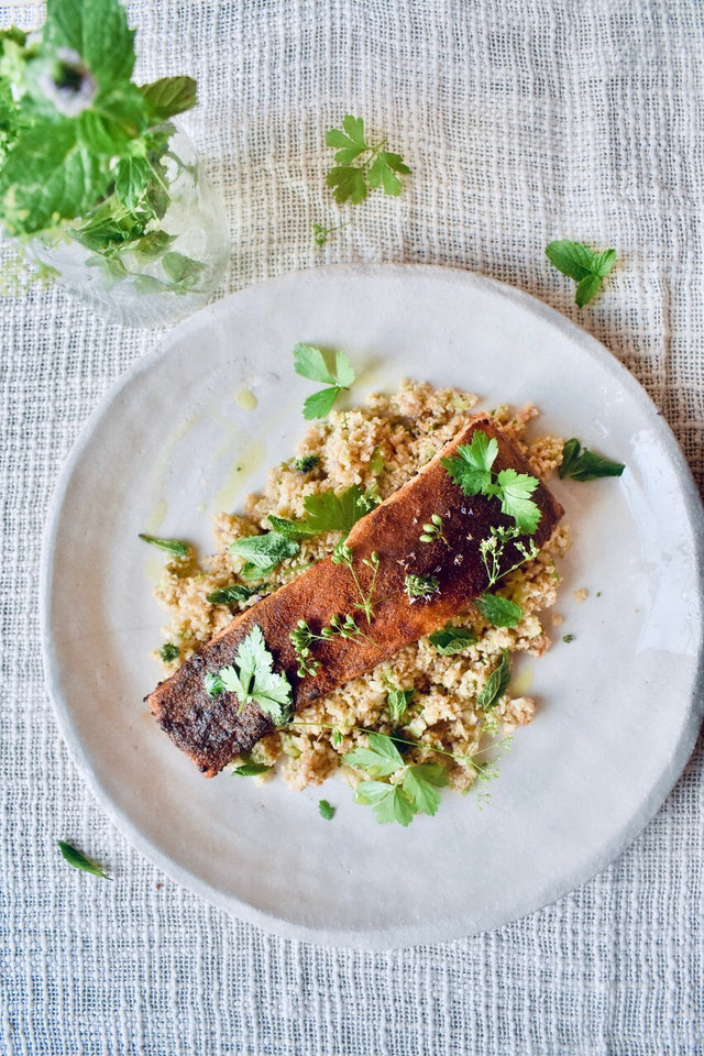 Grilled salmon fillet on a bed of couscous garnished with fresh green herbs on a white plate