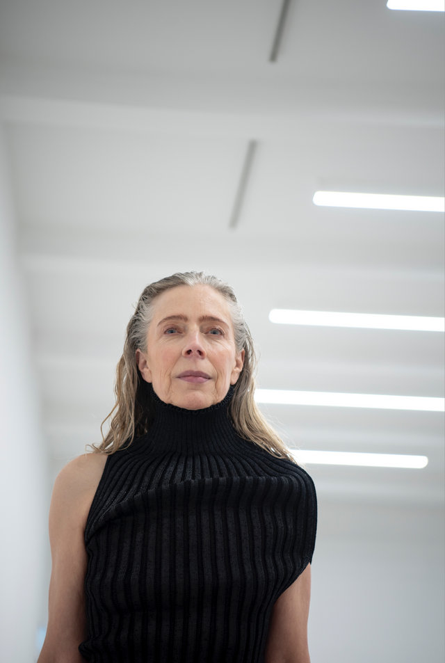 Sleeveless black ribbed knit top with high turtleneck collar, worn by model indoors