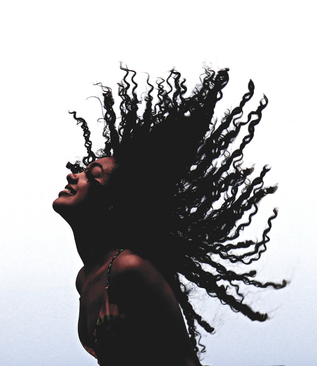 Woman with long, voluminous curly black hair flipping back against a white background