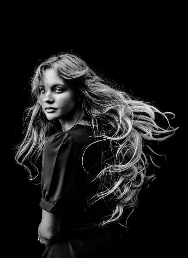 Black and white portrait of woman with long, wavy hair flowing and wearing a dark puff-sleeve top