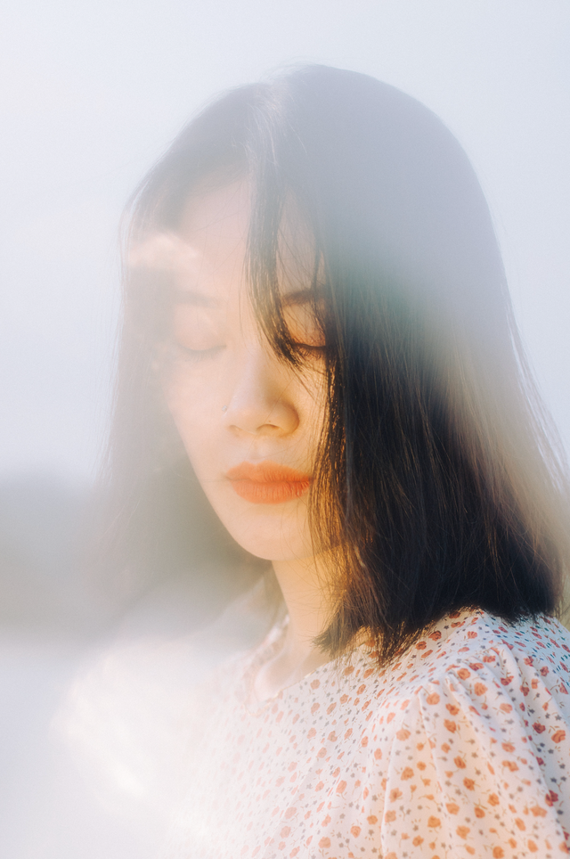 Woman with shoulder-length black hair wearing a white floral blouse with orange flowers