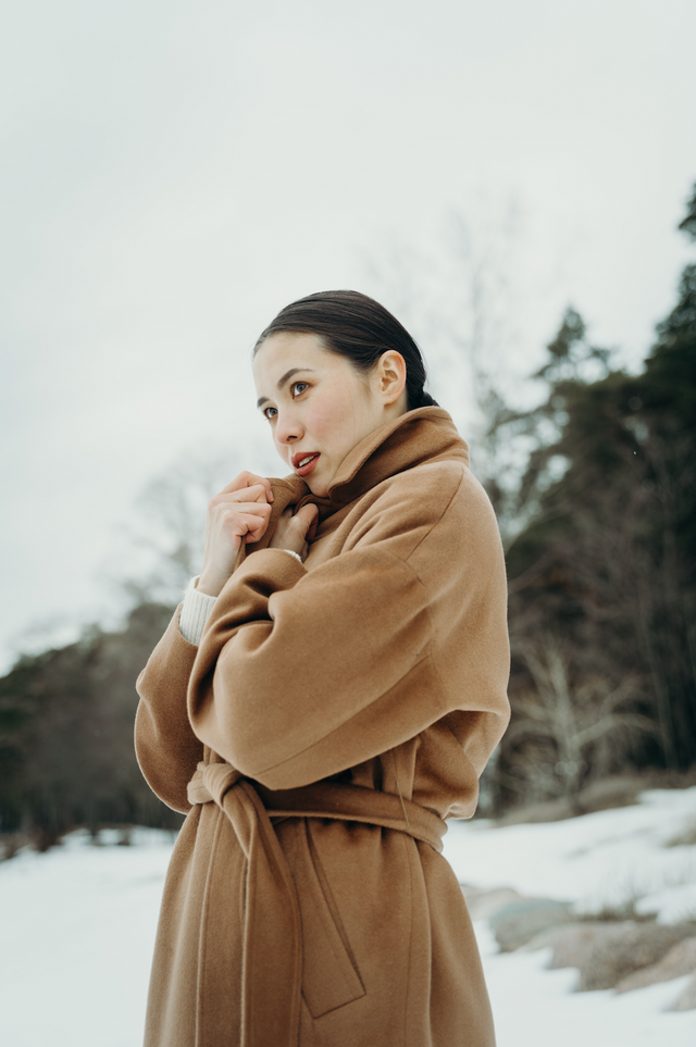 Woman wearing a belted camel brown wool coat outdoors in snowy winter landscape
