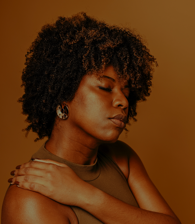 Woman with natural curly hair wearing a sleeveless olive green top and round tortoiseshell earrings