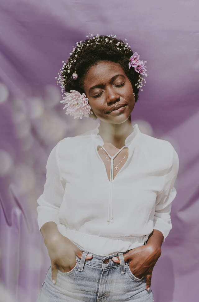 Woman with natural curly hair adorned with flowers, wearing a white blouse and denim jeans