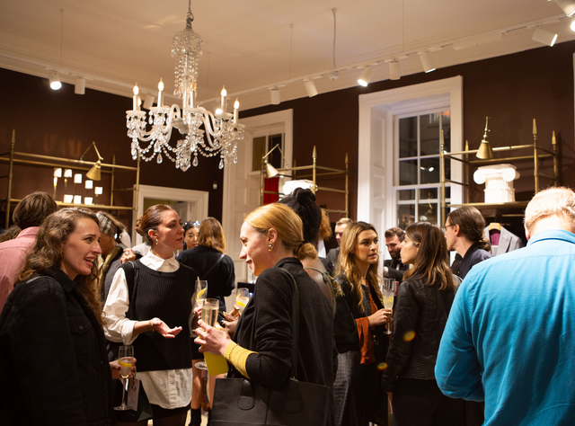 Group of people socialising indoors under a crystal chandelier, holding drinks in a warmly lit room