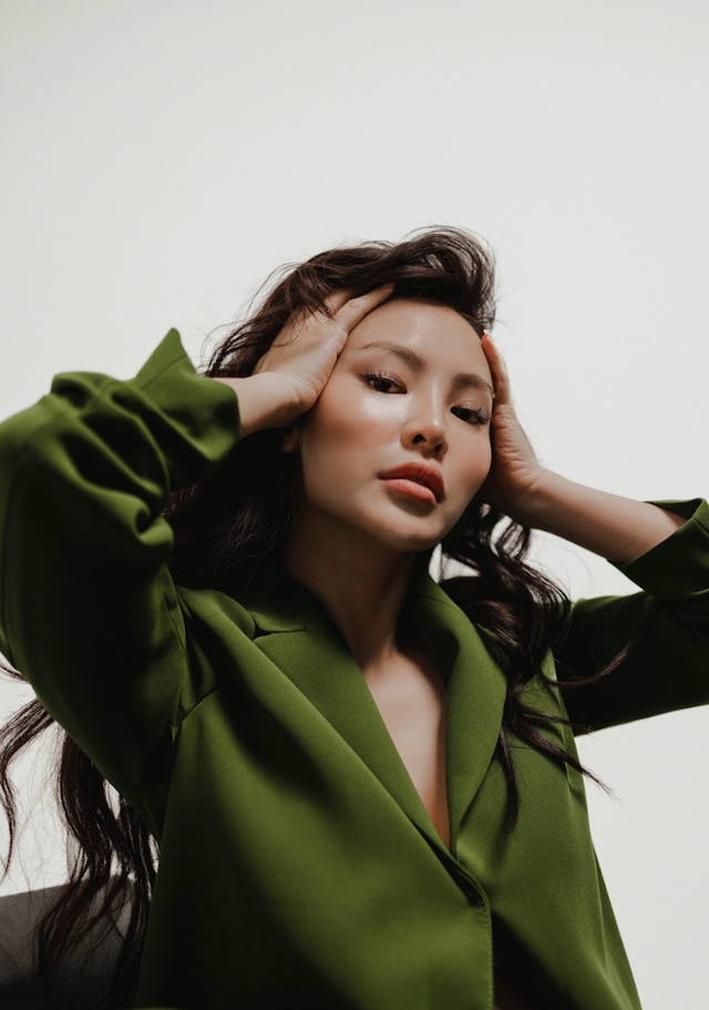 Woman with long dark hair wearing a green blazer, holding her head with both hands