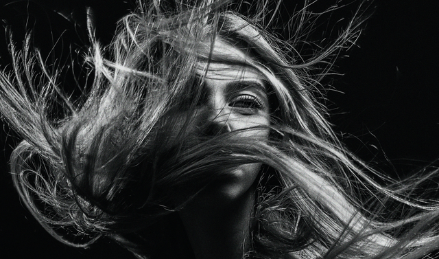 Black and white close-up of a woman with long hair flowing wildly against a dark background