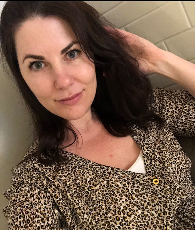 Woman with dark hair wearing a leopard print blouse and white top, touching her hair