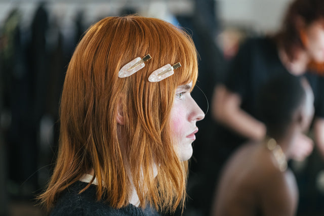 Red-haired model with shoulder-length hair wearing two large pearlescent hair clips on one side