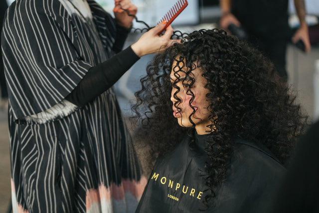 Stylist combing voluminous, tight black curls on model wearing black Monpure London cape