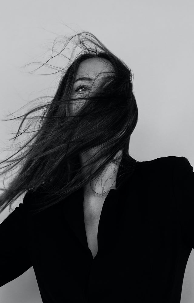 Black and white portrait of a woman with long flowing hair covering her face, wearing a black top