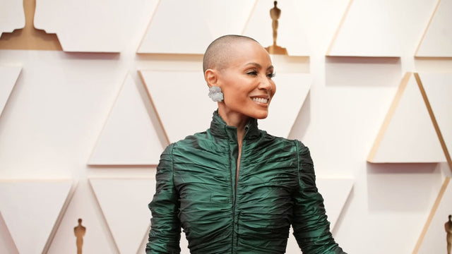 Smiling woman with shaved head wearing a ruched dark green dress and large silver earrings