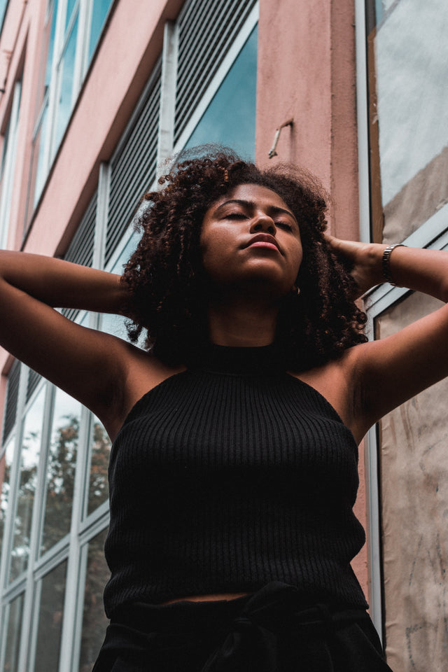 Woman with curly hair wearing a sleeveless black ribbed top outdoors by a building