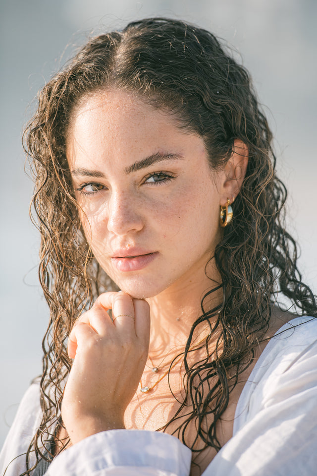 Woman with wet curly dark hair and natural skin wearing gold hoop earrings and delicate gold jewellery