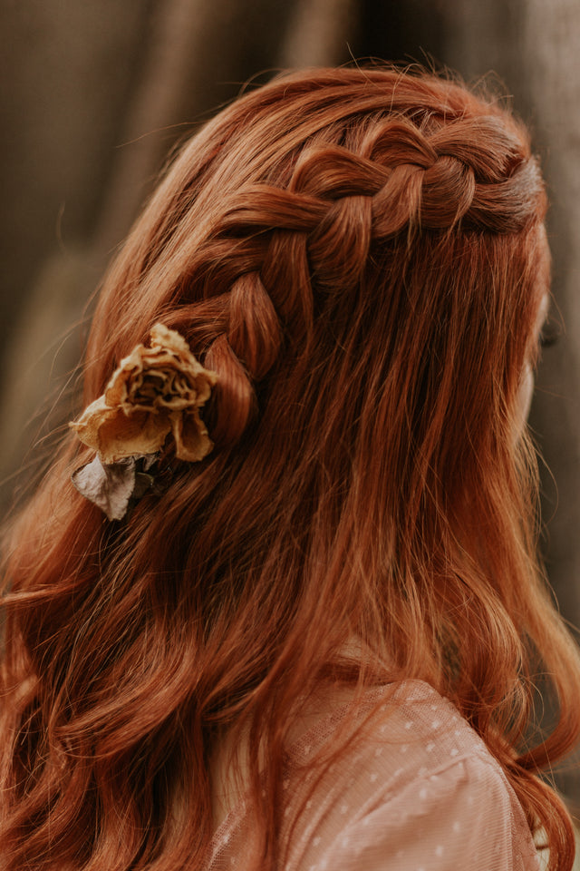 Red hair styled in a loose braid with a dried flower accessory on the side