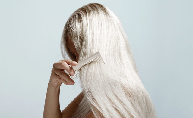 Person with long, straight, platinum blonde hair combing with a wide-tooth beige comb