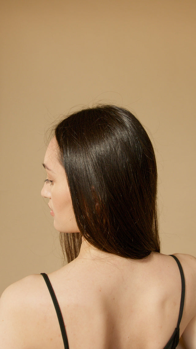 Woman with long, straight, shiny dark brown hair wearing a black spaghetti strap top