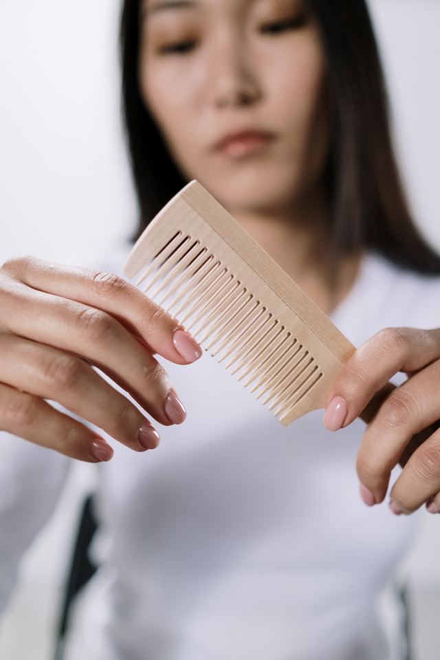 Woman holding a light wooden comb with fine teeth, focusing on the comb in her hands
