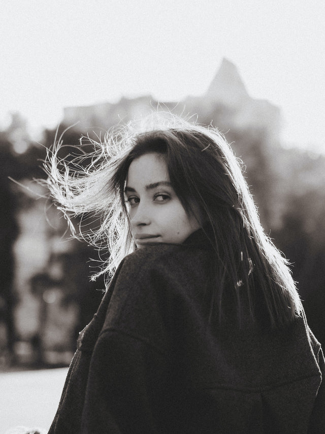 Young woman with long hair wearing a dark coat outdoors with sunlight highlighting hair strands