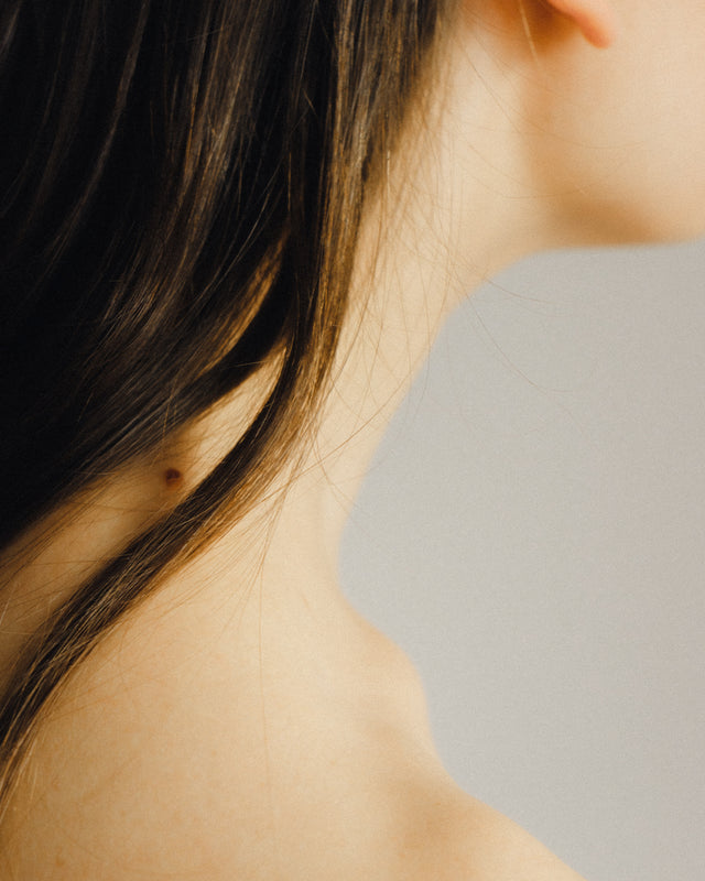 Close-up of fine, dark brown hair strands against pale skin and neutral background