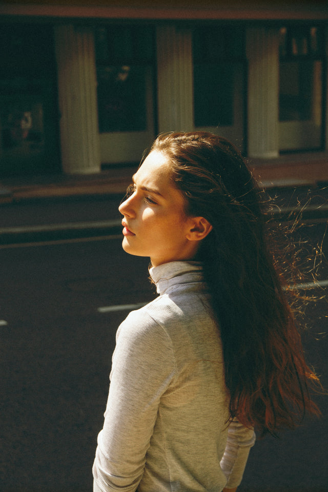 Young woman with long brown hair wearing a light grey turtleneck top outdoors