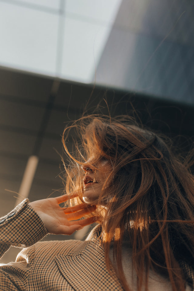 Woman with long auburn hair blowing in the wind wearing a checkered blazer outdoors
