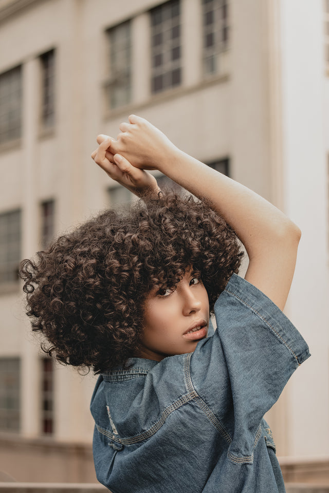 Person with voluminous curly dark hair wearing a blue denim jacket outdoors