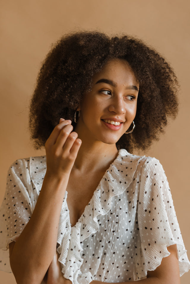 Young woman with voluminous curly hair wearing a white polka dot blouse smiling confidently