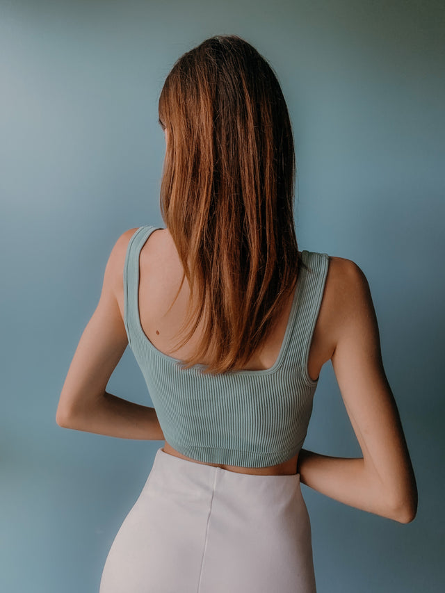 Woman with long brown hair wearing a ribbed pale green crop top and white high-waisted skirt