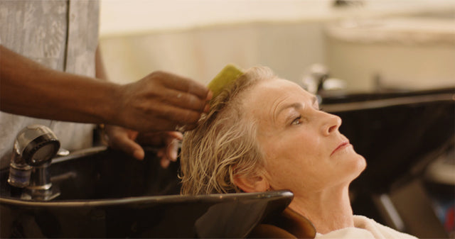 Person receiving scalp massage with a green comb at a salon wash basin