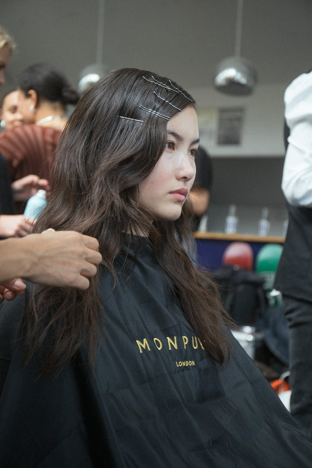 Young woman with long dark wavy hair styled with silver hair clips, wearing a black Monpure London cape