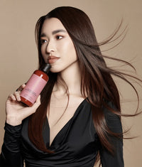 Woman with long dark hair holding a brown bottle with pink label Ceramide Complex Bond Repair Conditioner