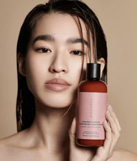 Woman holding brown bottle with pink label of Ceramide Complex Bond Repair Conditioner