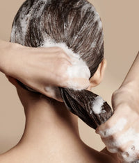 Person washing long dark hair with foamy shampoo, hands massaging scalp and hair