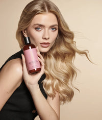 Blonde woman with wavy hair holding brown bottle of Ceramide Complex Bond Repair Shampoo with pink label