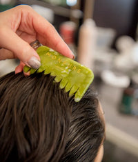 Green jade comb with gold lettering being used on dark wet hair for healing and energising