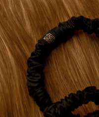 Set of slim black silk scrunchies with gold embroidery on a wooden surface