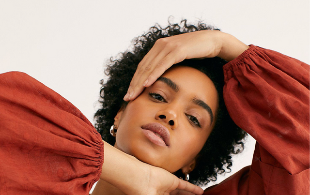 Close-up of woman with natural curly hair wearing a rust-coloured long sleeve blouse
